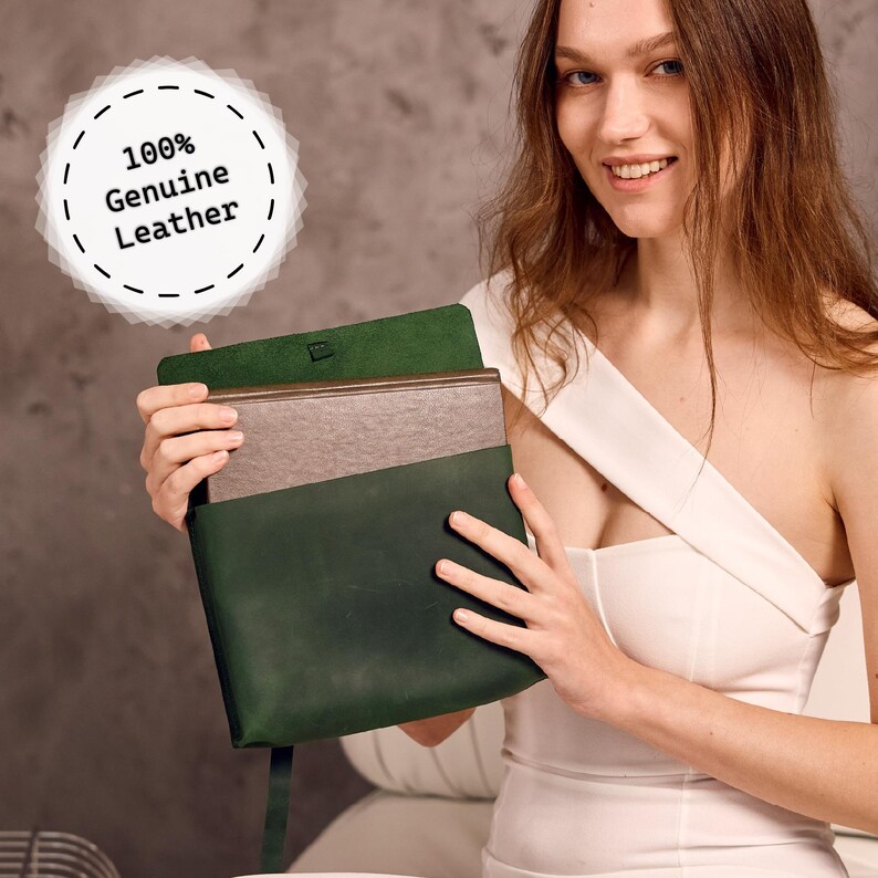 May include: A dark green leather portfolio with a flap closure, holding a light brown item. The text "100% Genuine Leather" is displayed on a white circular label. The portfolio is held open, showcasing the interior.