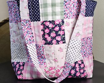 May include: A patchwork tote bag with various fabric patterns. The bag features squares of floral, polka dot, and gingham fabrics in pink, white, and navy blue. It has a matching strap.