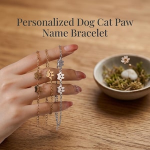 May include: Three delicate chain bracelets featuring small paw print charms. Two bracelets are gold-toned and one is silver-toned. The text Personalized Dog Cat Paw Name Bracelet is visible at the top of the image above the jewelry items.