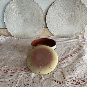Könnte beinhalten: Zwei runde, gewebte Tischsets mit gewelltem Rand. Eine Keramikschale mit Deckel mit einem Sternmuster in Braun- und Gelbtönen. Die Schale hat einen braunen Innenraum und einen hellblauen Außenraum.