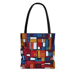 Pode incluir: Uma sacola com alça preta e um padrão geométrico colorido. O padrão apresenta uma mistura de formas retangulares vermelhas, azuis, amarelas e brancas. A sacola é projetada para transportar itens e tem uma estética simples e moderna.
