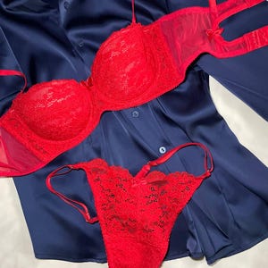 May include: A red lace bra and matching thong set with delicate details, resting on a navy blue satin shirt. The bra features underwire support and adjustable straps. The lingerie set is designed with a romantic aesthetic.