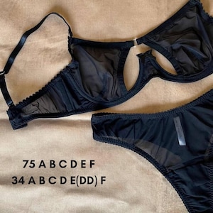 Könnte beinhalten: Schwarzes Dessous-Set mit einem transparenten BH mit verstellbaren Trägern und einem passenden Slip. Der BH hat ein einzigartiges Cut-Out-Design. Das Set ist aus zartem, durchsichtigem Stoff gefertigt. BH-Größen sind 75 A B C D E F und Slip-Größen sind 34 A B C D E(DD) F.