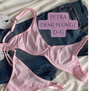 May include: A light pink demi plunge bra and matching panty set featuring a subtle vertical ribbed texture and delicate scalloped edges. The bra includes adjustable straps and underwire support. Text on the image reads PETRA DEMI PLUNGE D-G.