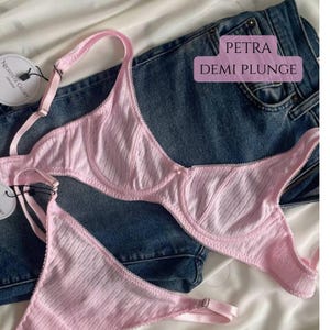 May include: A light pink demi plunge bra and matching underwear set with a striped pattern. The lingerie is displayed on a pair of blue denim jeans. The text "PETRA DEMI PLUNGE" is visible.