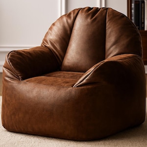 May include: A brown leather beanbag chair with a rounded back and armrests. The chair is made of a soft, textured material and sits on a light-coloured rug. The chair is designed for comfort and relaxation.