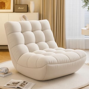 Puede incluir: Un sillón de salón color crema, acolchado, con base redondeada. La silla tiene un perfil bajo y un asa en la parte trasera. Se encuentra sobre una alfombra redonda de color blanco roto. Una revista y unos auriculares están sobre la alfombra.