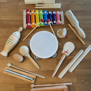 Può includere: Una collezione di strumenti musicali in legno che include uno xilofono multicolore con due bacchette, un tamburello rotondo, un guiro a forma di pesce, un blocco di legno, uno shaker, nacchere, una barra sonora e vari bastoncini e battenti.