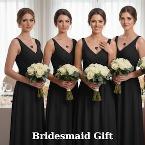 Puede incluir: Cuatro personas con vestidos negros sin mangas de cuello en V idénticos, cada una sosteniendo un ramo de rosas blancas con follaje verde. Cada persona lleva un collar con un colgante azul oscuro en forma de corazón. Texto: Bridesmaid Gift.