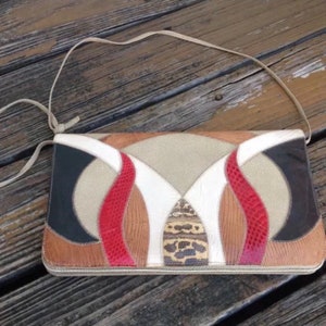 May include: A geometric patchwork clutch bag made of different colored leathers. The bag has a long strap and is made of brown, black, white, red, and beige leather.