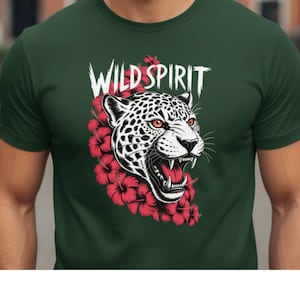 Puede incluir: Camiseta verde oscuro con una ilustración de la cabeza de un jaguar, con la boca abierta, rodeada de flores de hibisco rojas. El texto "WILD SPIRIT" está encima del jaguar. El diseño es en negro, blanco y rojo. Una camiseta gráfica audaz.