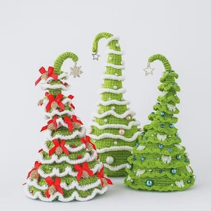 Könnte beinhalten: Drei handgefertigte gehäkelte Weihnachtsbäume in verschiedenen Größen. Die Bäume sind grün mit weißen Akzenten, verziert mit roten Schleifen, Perlen und sternförmigen Ornamenten. Das skurrile Design verleiht der Weihnachtsdekoration eine festliche Note.
