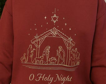 May include: Burgundy sweatshirt with a gold-colored illustration of the Nativity scene, including the Holy Family, animals, and stars. The text "O Holy Night" is printed below the illustration.
