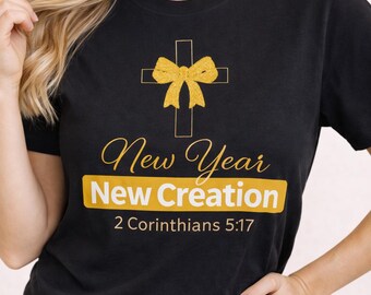 May include: Black t-shirt featuring a gold cross and bow graphic. The words "New Year New Creation" are in gold, with the Bible verse 2 Corinthians 5:17 underneath. The shirt has a crew neck.