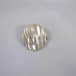 Può includere: Un fermaglio rotondo argentato con un design ondulato e testurizzato.