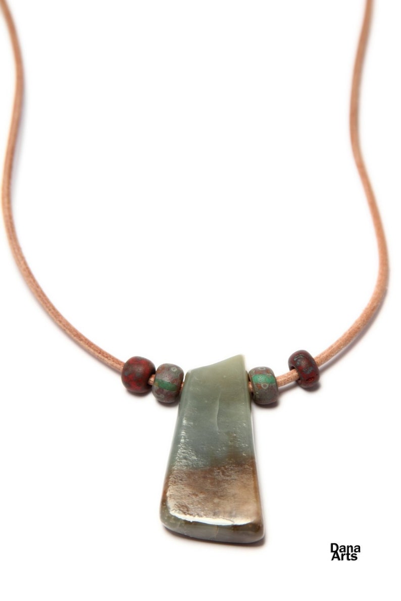May include: A green stone pendant with brown and red beads on a brown leather cord.