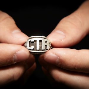 May include: A silver ring with the letters "CTR" engraved on the top.