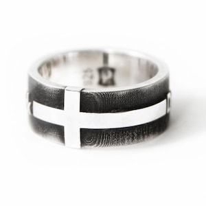 May include: A silver ring with a black oxidized finish and a white cross design. The ring is engraved with the words "Faith" and "Hope".