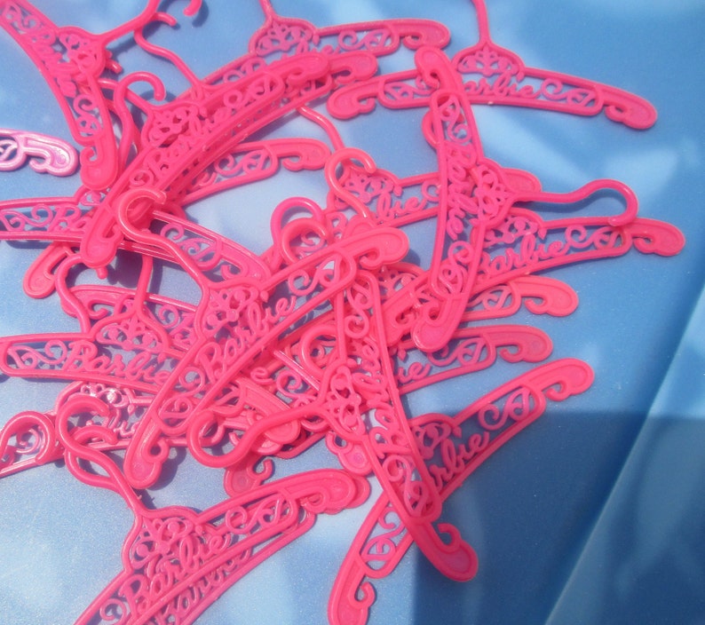 Op de afbeelding: Een stapel roze plastic hangers met het woord "Barbie" erop gedrukt.