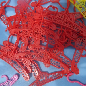 Op de afbeelding: Een stapel rode plastic hangers met het woord "Barbie" erop gegraveerd.
