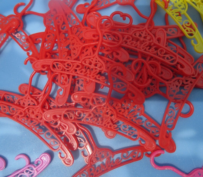 Op de afbeelding: Een stapel rode plastic hangers met het woord "Barbie" erop gegraveerd.