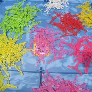 Op de afbeelding: Een grote verzameling plastic hangers in verschillende kleuren, waaronder geel, groen, roze en wit. De hangers bevinden zich allemaal in een plastic opbergdoos.