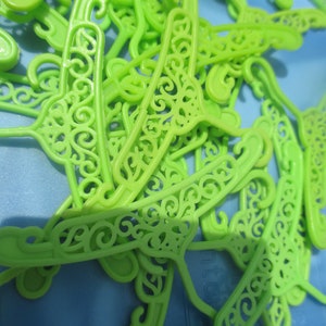 Op de afbeelding: Een stapel felgroene plastic hangers met een decoratief, versierd ontwerp. De hangers zijn gemaakt van lichtgewicht plastic en hebben een gladde, glanzende afwerking.