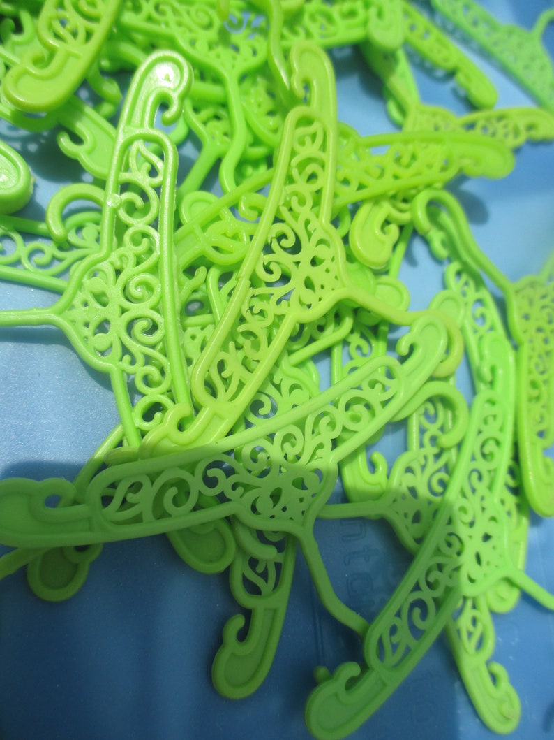 Op de afbeelding: Een stapel felgroene plastic hangers met een decoratief, versierd ontwerp. De hangers zijn gemaakt van lichtgewicht plastic en hebben een gladde, glanzende afwerking.