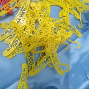 Op de afbeelding: Een stapel gele plastic hangers met een decoratief ontwerp. De hangers liggen op een blauwe ondergrond.