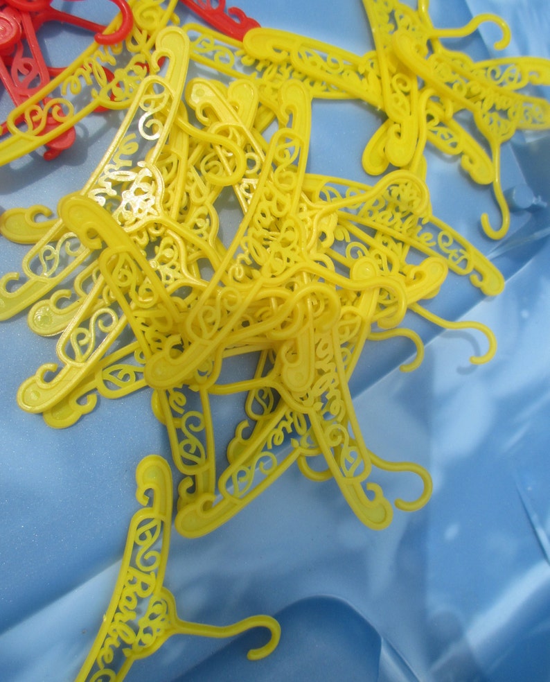 Op de afbeelding: Een stapel gele plastic hangers met een decoratief ontwerp. De hangers liggen op een blauwe ondergrond.