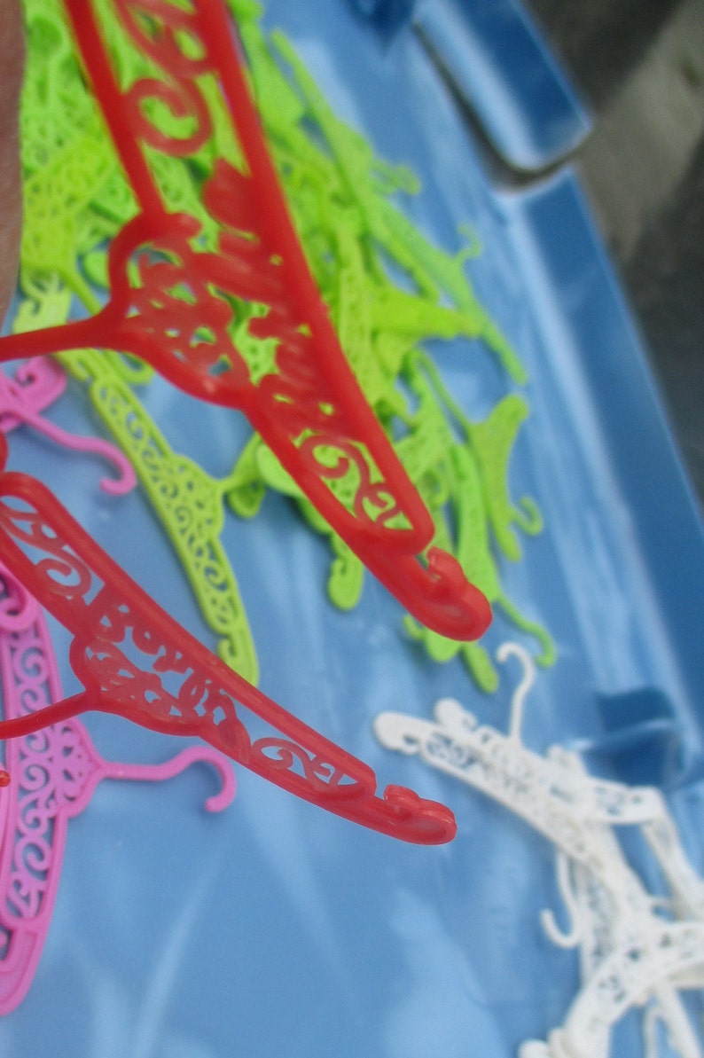 Op de afbeelding: Een close-up van een stapel kleurrijke plastic hangers. De hangers zijn in verschillende vormen en maten, waaronder sommige met decoratieve ontwerpen. De hangers liggen op een blauw oppervlak.