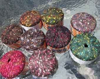 May include: Eight spools of sparkly yarn in various colors, including red, green, gold, and black. The yarn is wrapped around cardboard spools with labels.