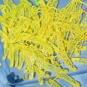 Op de afbeelding: Een stapel gele plastic hangers met decoratieve details. De hangers zijn willekeurig gerangschikt en allemaal even groot en even gevormd.
