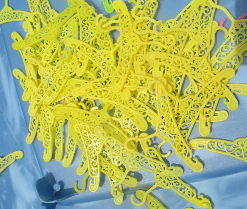 Op de afbeelding: Een stapel gele plastic hangers met decoratieve details. De hangers zijn willekeurig gerangschikt en allemaal even groot en even gevormd.