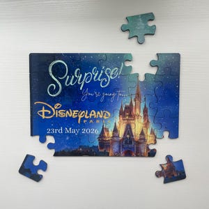 Puede incluir: Un rompecabezas parcialmente ensamblado con las palabras "Surprise! You're going to... Disneyland Paris 23rd May 2026" sobre un fondo de cielo estrellado. El rompecabezas presenta una imagen de castillo y varias piezas sueltas.