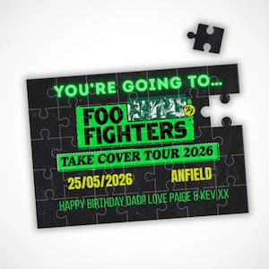 May include: A black jigsaw puzzle with a missing piece. The puzzle features the text "YOU'RE GOING TO... FOO FIGHTERS TAKE COVER TOUR 2026 25/05/2026 ANFIELD HAPPY BIRTHDAY DAD!! LOVE PAIGE & KEV XX" in green and white.