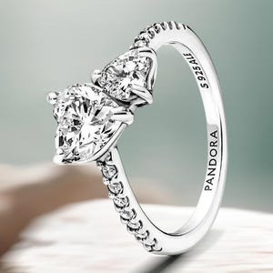 Peut inclure: Une bague en argent ornée de deux pierres précieuses claires en forme de poire. La monture est ornée de petites pierres claires sur un côté et porte l'inscription "PANDORA" et "S925 ALE" à l'intérieur.