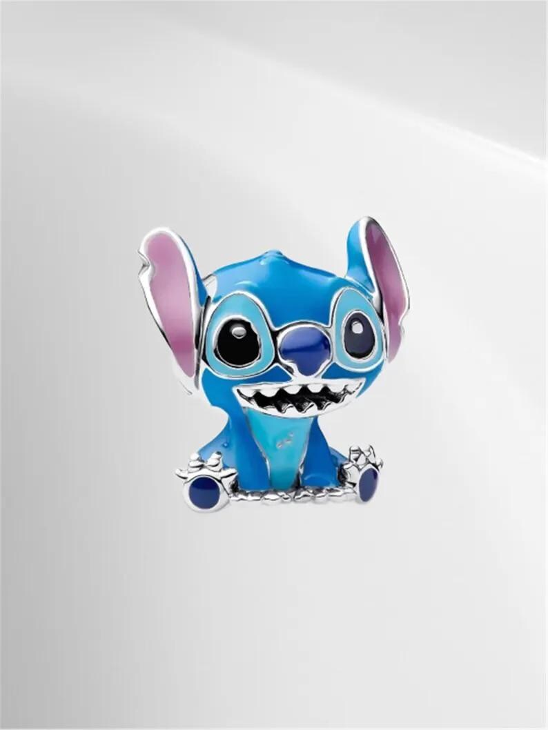 May include: A blue and silver charm featuring the character Stitch from the Disney movie Lilo & Stitch. The charm has large black eyes, a wide grin, and large ears with pink inner ears. The charm is made of metal and enamel.