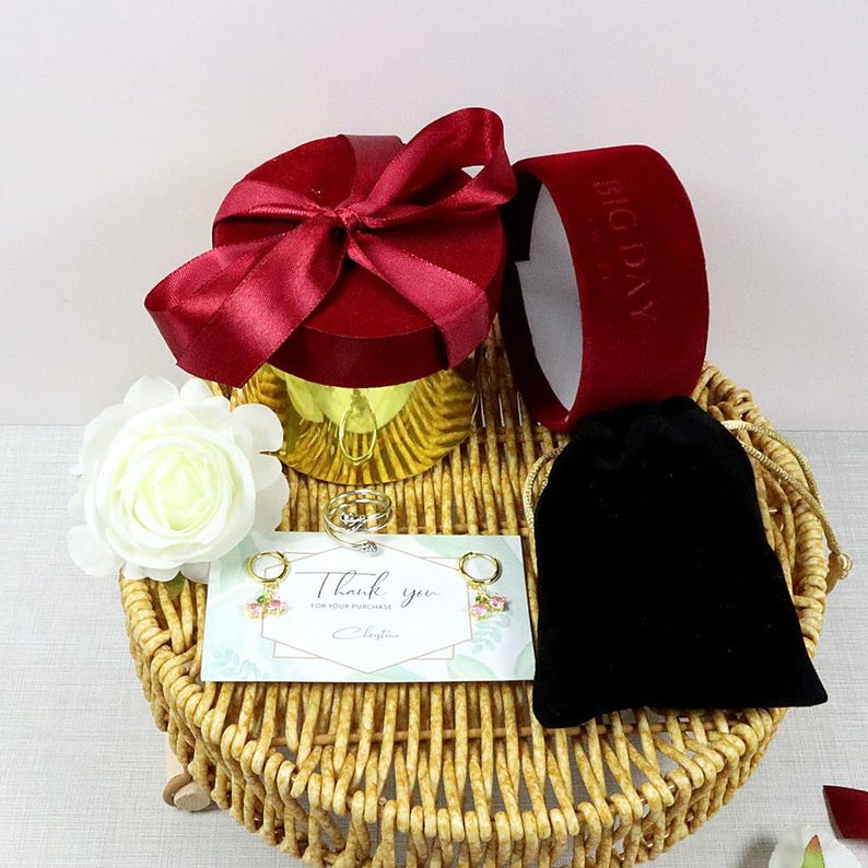 May include: A gift set with a red velvet box and ribbon, a white rose, a black velvet pouch, and a woven basket. Includes a ring, earrings, and a card that says "Thank you."