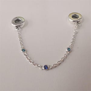 Può includere: Catena di sicurezza per bracciale con ciondoli in argento con tre pietre blu. La catena ha due terminali circolari con la scritta "S925 ALE". Le pietre preziose sono un mix di blu chiaro e scuro.