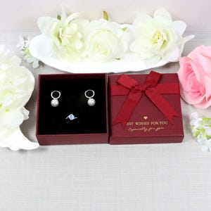 May include: A jewelry set featuring a pair of pearl earrings and a ring with a blue gemstone, presented in a red gift box with a bow. The box has the text "BEST WISHES FOR YOU Especially for you."