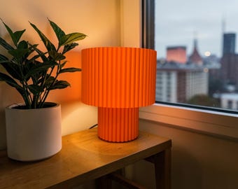 Lámpara de mesa plisada de color naranja vibrante, estilo retro pop art de los años 70.