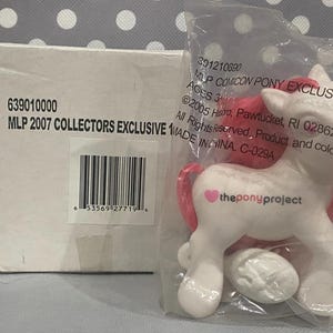 Puede incluir: Un pony blanco con pelo rosa y un símbolo en forma de corazón en su costado. El pony es parte de un set exclusivo de colección My Little Pony de 2007. El empaque incluye el texto "MLP 2007 COLLECTORS EXCLUSIVE" y "theponyproject".