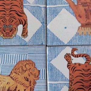 Può includere: Quattro piastrelle blu e bianche con motivi con illustrazioni di tigri arancioni. Le tigri sono in diverse pose, tra cui una tigre con la testa capovolta, una tigre con la coda arrotolata e una tigre con le zampe alzate. Le piastrelle fanno parte di un set più grande.