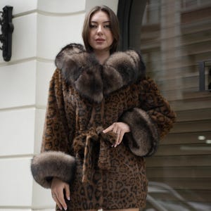 May include: A brown and black leopard print coat with a fur collar and cuffs. The coat is belted at the waist and has a luxurious appearance. The model is wearing the coat in an outdoor setting.