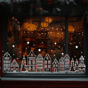 Könnte beinhalten: Fensterdekoration mit weißer Umrisszeichnung einer winterlichen Dorfszene mit Häusern, Bäumen und Sternen. Der Hintergrund zeigt ein warmes Interieur mit Lichtern und Dekorationen, das eine festliche Atmosphäre schafft.