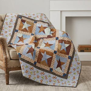 May include: A patchwork quilt featuring a repeating star pattern in shades of brown, tan, and light blue. The quilt has a border with a small owl print on a light blue background and is draped over a beige upholstered armchair with wooden legs.