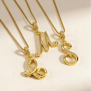 Peut inclure: Colliers avec initiales dorées. Les lettres L, M et S sont présentées, chacune avec une chaîne délicate. Les pendentifs sont ornés de petits cristaux étincelants. Les bijoux sont posés sur un fond doux et neutre.