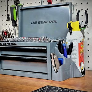 May include: A gray US General tool chest with two drawers and a top compartment. The chest has the brand name printed on the front. A variety of tools are visible, including sockets, screwdrivers, and pliers. A can of lubricant and a tool organizer are also present.