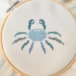 May include: A blue and gray cross-stitch embroidery of a crab in a wooden embroidery hoop.